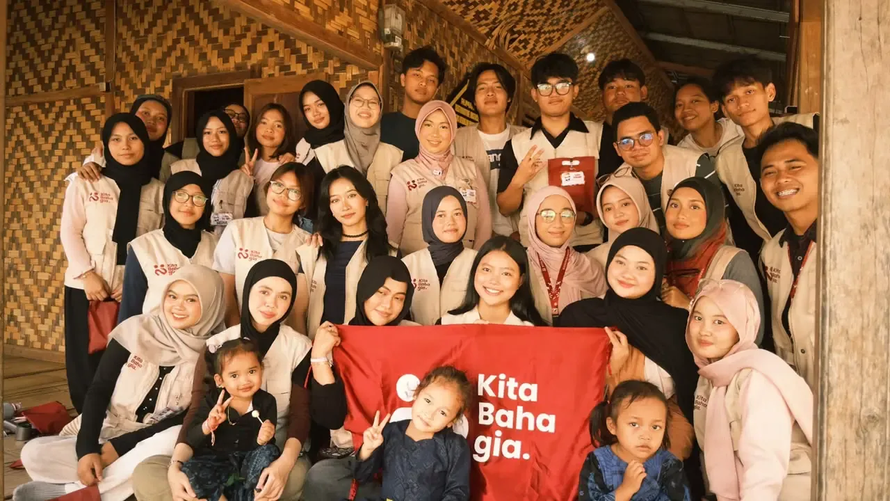 Relawan Kita Bahagia berfoto bersama warga sambil membentangkan bendera Kita Bahagia